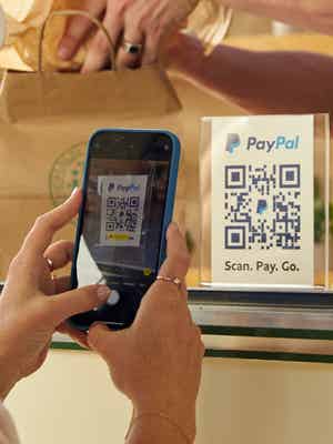 Person using their phone to scan a PayPal QR code on a window